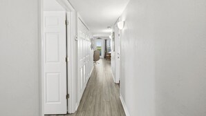 A hallway with white walls and wooden flooring, leading to a dining area with chairs and a table. - The Skimmer Condo: Downtown on the Bay - Nature Views - Bird watching (Cedar Key)