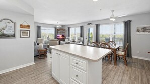 A spacious kitchen with a central island, dining area with chairs, and a TV. - The Skimmer Condo: Downtown on the Bay - Nature Views - Bird watching (Cedar Key)