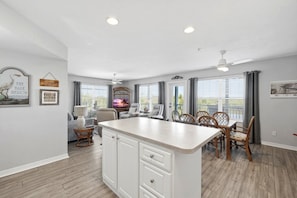 A spacious kitchen with a central island, dining area with chairs, and a TV.