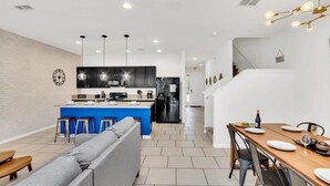 A modern kitchen with a blue island, a dining area with a wooden table, and a living area with a grey sofa. - Private Views & Theme Rooms, Perfect for Families! (Davenport)