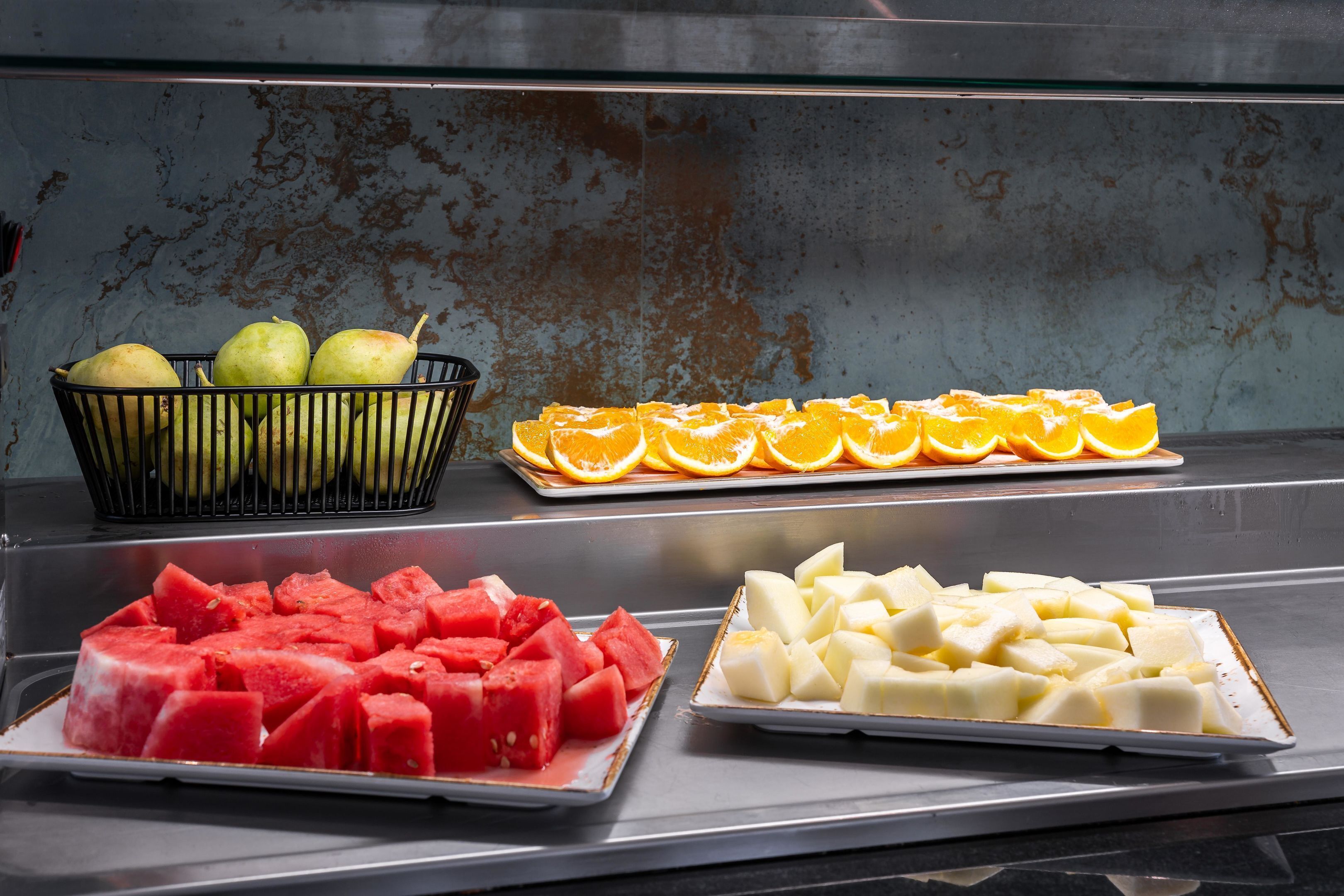 A buffet with various fruits including watermelon, oranges, and pears.