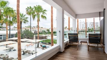 Un balcón moderno de hotel con suelo de madera, ventanas grandes y mobiliario exterior.