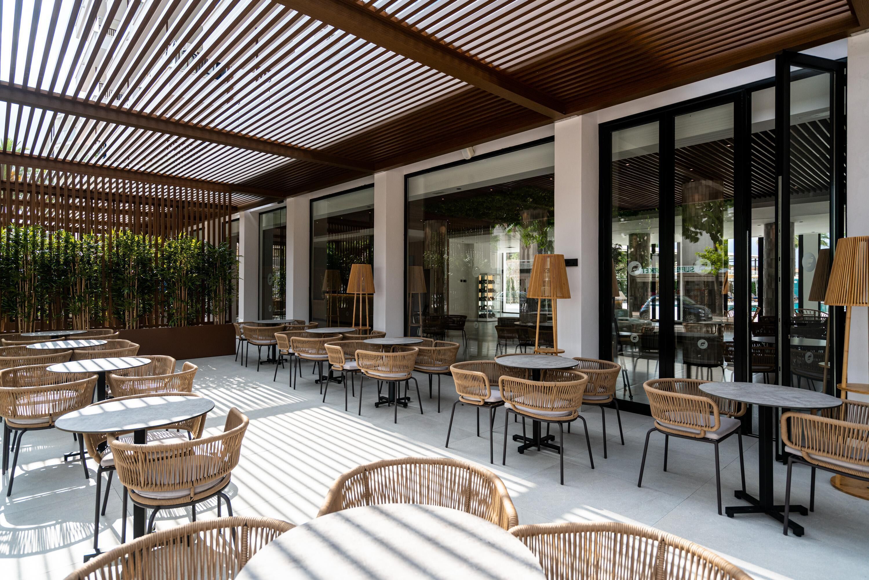 Un área de café al aire libre con mobiliario de mimbre y ventanas grandes.