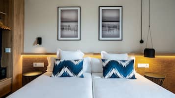 Una cama doble con ropa de cama blanca y dos almohadas estampadas en azul y blanco. Encima de la cama hay dos cuadros enmarcados en la pared.