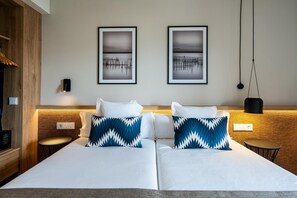 Una cama doble con ropa de cama blanca y dos almohadas estampadas en azul y blanco. Encima de la cama hay dos cuadros enmarcados en la pared.