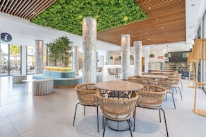 Un espacio interior moderno con mesas redondas y sillas de mimbre, una pared verde y techo de madera.