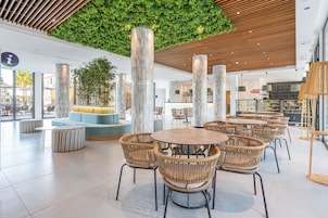 Un espacio interior moderno con mesas redondas y sillas de mimbre, una pared verde y techo de madera.