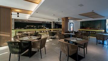 Un restaurante moderno con mesas y sillas altas, una zona de bar y vistas a la ciudad.