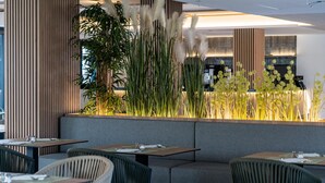 A modern restaurant with a seating area featuring cushioned benches and tables, surrounded by tall plants and decorative grasses. - THB Bamboo Alcudia Hotel - Adults Only (Alcúdia)