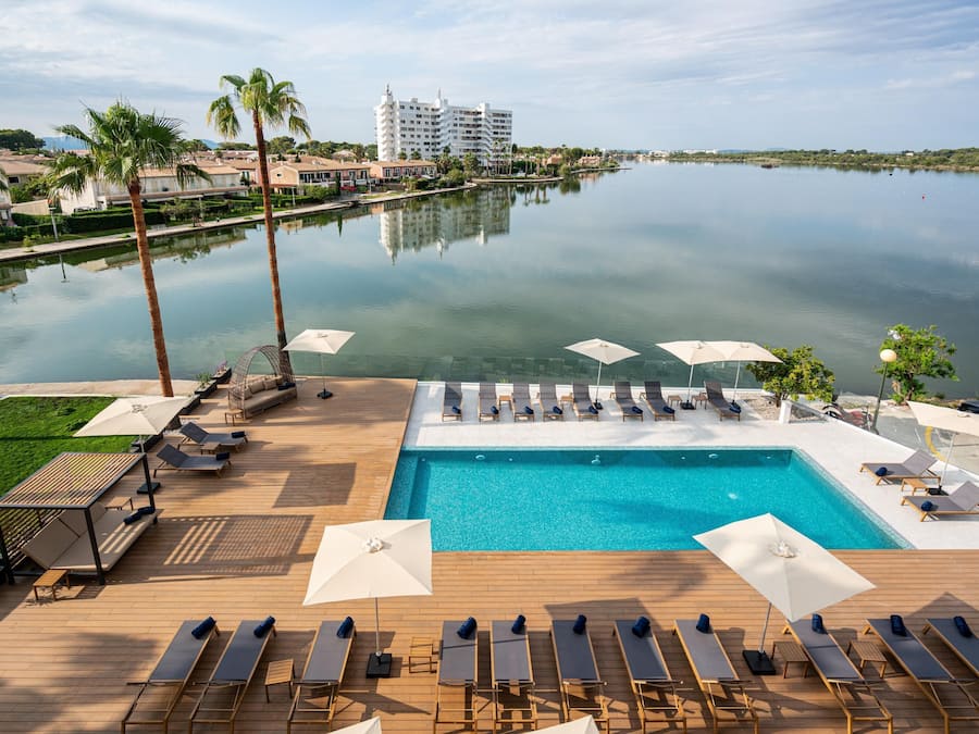 Zona de piscina con sillones de descanso, sombrillas y vistas al agua y edificios.