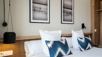 A hotel room with a bed, two framed pictures on the wall, a hanging light, and a wooden headboard.