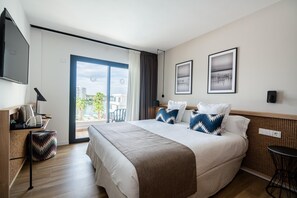 Habitación de hotel moderna con una cama grande, un escritorio con lámpara, una silla y vistas al exterior.