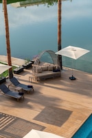 A wooden deck with lounge chairs, a wicker sofa, and umbrellas by a calm body of water.