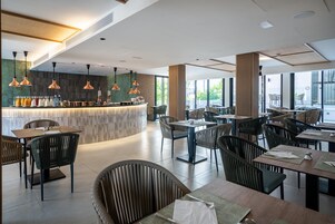 A modern restaurant with a bar area, multiple dining tables, and chairs.