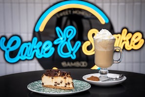 Uma fatia de cheesecake e um milkshake sobre uma mesa, com um letreiro de neon ao fundo.