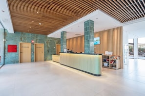 Un espace d’accueil moderne avec un plafond en bois, un comptoir d’accueil et un téléviseur fixé au mur.