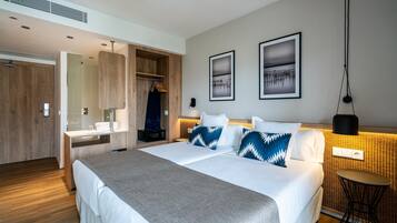 Una habitación de hotel moderna con una cama grande, un armario de madera, una cómoda con espejo y dos cuadros en la pared.