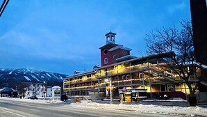 Ein Gebäude mit einem Glockenturm, einem mit Lichtern beleuchteten Balkon und einer verschneiten Straße.