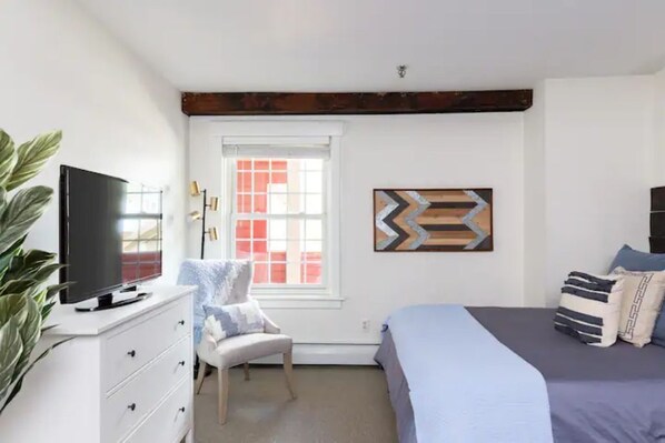 A bedroom with a bed, a chair, a TV on a dresser, and a window with blinds. - Okemo's Back Room - in the heart of the village on the shuttle route! (Ludlow)
