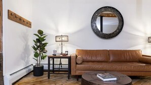 Ein Wohnzimmer mit einem braunen Ledersofa, einem runden Spiegel, einem kleinen Tisch mit Lampe und einem Blumentopf.