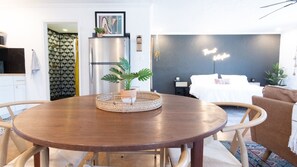Een moderne woonkamer met een ronde houten tafel, een bed met witte beddengoed en een blauw accentmuur.