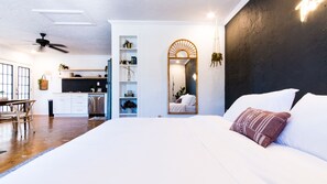 Een moderne slaapkamer met een groot bed, een spiegel en uitzicht op de keuken.