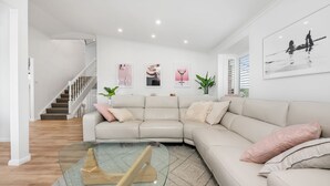 Uma sala de estar moderna com um sofá modular bege, uma mesa de centro de vidro e uma escada que leva a outro andar.