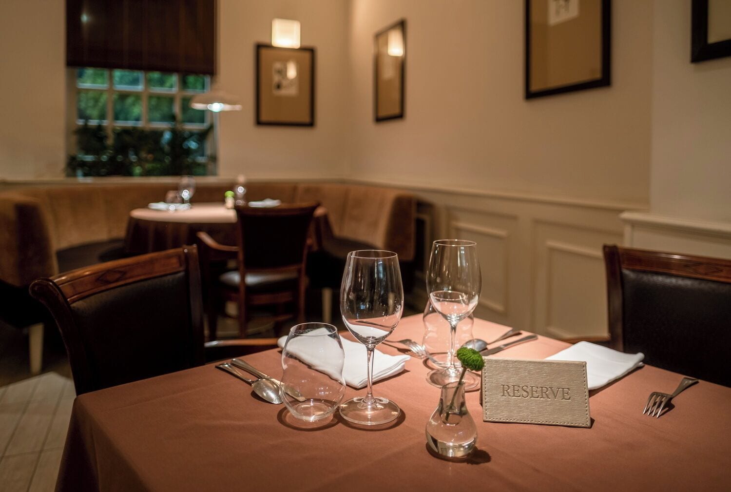 A dining table set with wine glasses, a vase with a green plant, and a 'RESERVE' sign.