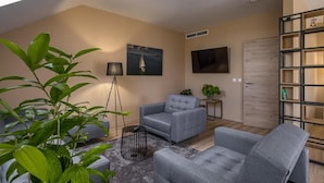 A modern living room with a grey sofa, a small side table, a floor lamp, and a bookshelf. - Kistücsök Food & Room (Balatonszemes)