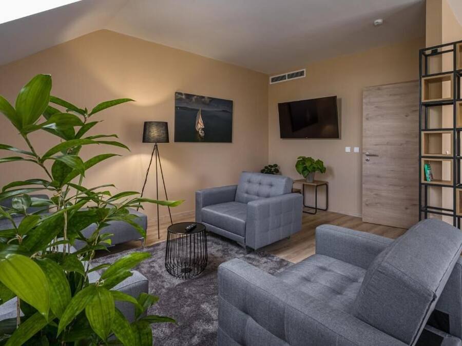 Un salon moderne avec un canapé gris, une petite table d’appoint, une lampe sur pied et une bibliothèque.