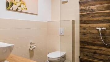 A modern bathroom with a wooden wall, a glass shower enclosure, a toilet, and a sink with toiletries.