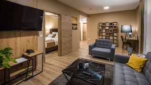 A modern living room with a flat-screen TV, a sofa, a coffee table, and a workspace with a desk and chair. - Kistücsök Food & Room (Balatonszemes)