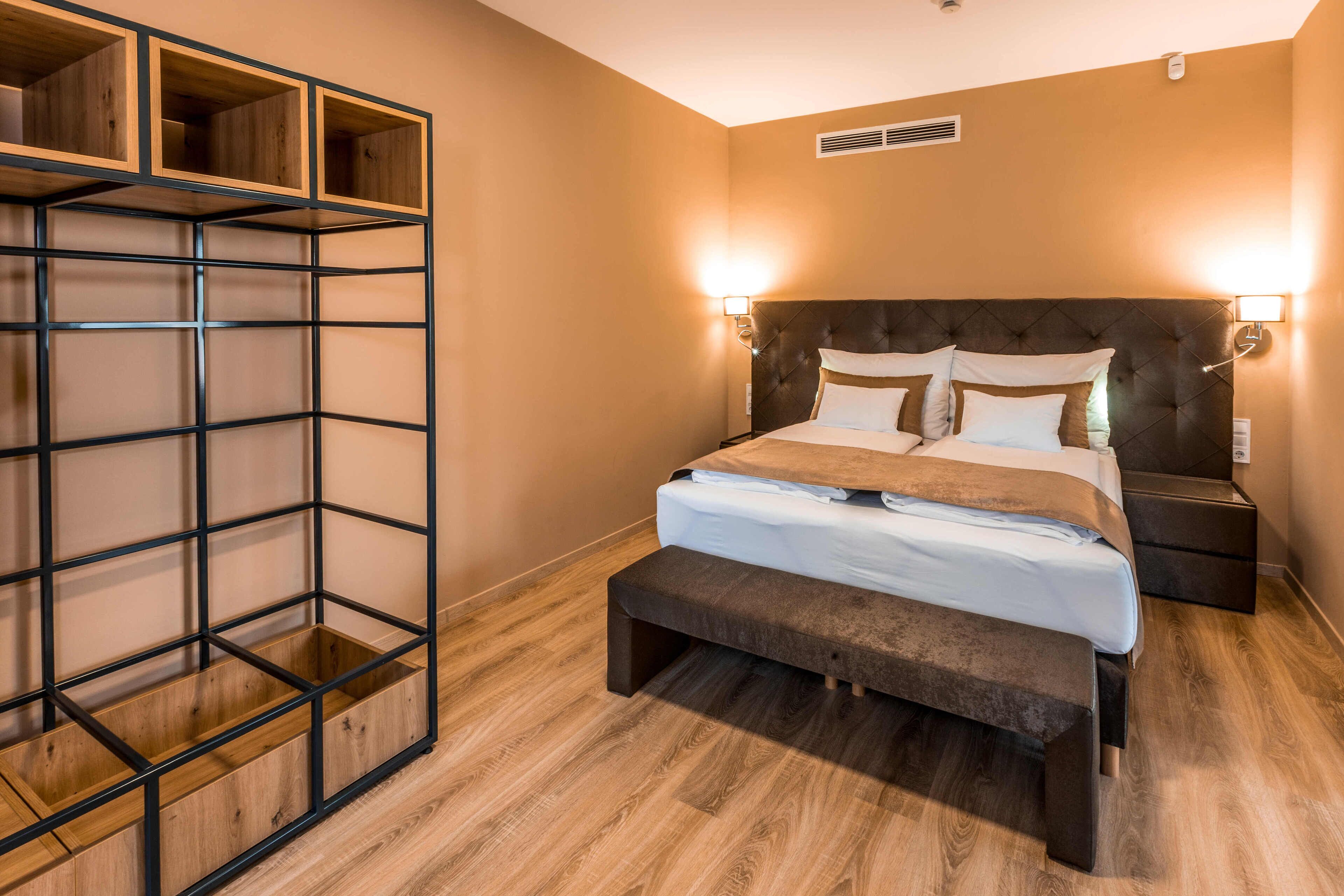 Une chambre à coucher comprenant un lit, des tables de chevet, un banc et une étagère.