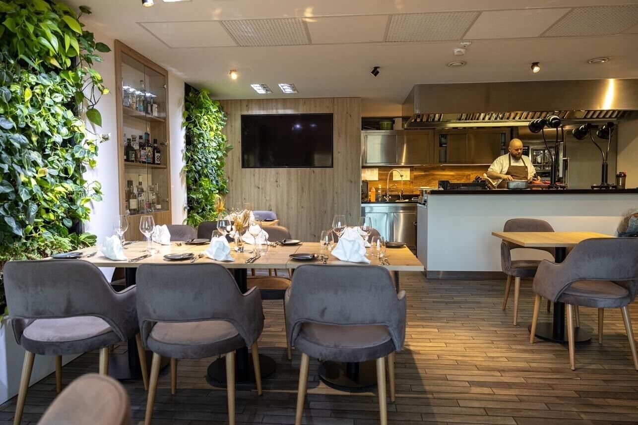 A modern restaurant with a wooden interior, a bar area, and a chef preparing food.
