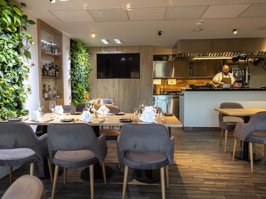 A modern restaurant with a wooden interior, a bar area, and a chef preparing food.