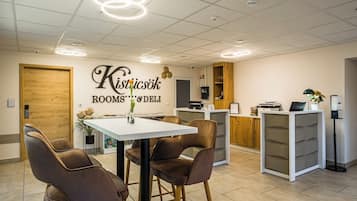 A modern hotel room with a white table, two brown chairs, a wooden door, and a sign reading "Kisticsök ROOMS & DELI".
