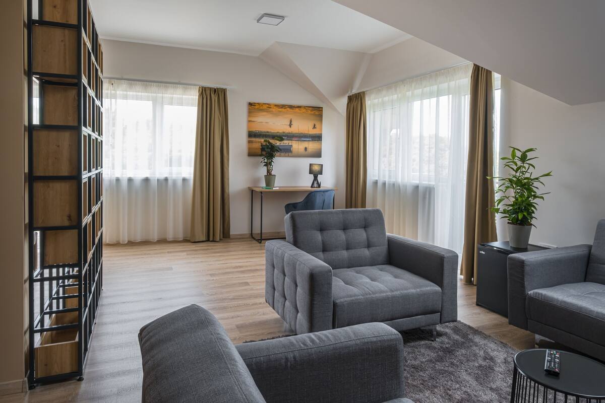 A modern living room with a sofa, armchairs, a coffee table, a bookshelf, and a painting on the wall.