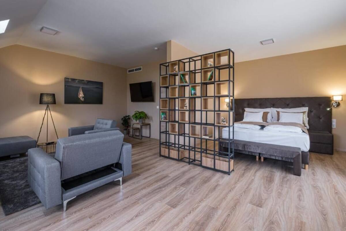 A modern hotel room with a sofa, a bed, a TV, and a bookshelf.