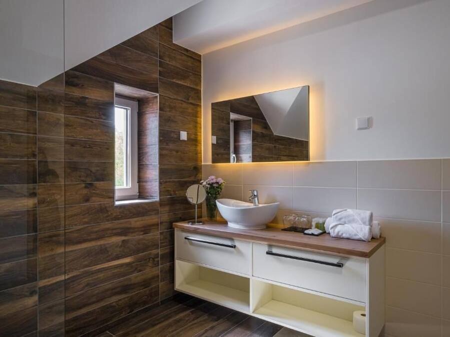 Un baño moderno con pared de madera, un espejo grande, un lavabo blanco y un mueble de tocador con cajones.