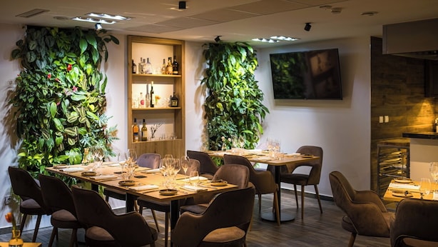 A dining area with two tables set for six, surrounded by chairs. There are vertical gardens on the walls, a wooden shelf with bottles, and a television mounted on the wall. - Kistücsök Food & Room (Balatonszemes)