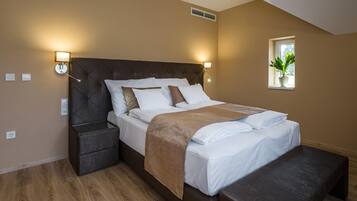 A bedroom with a large bed, bedside tables, a bench, and a window with a plant.