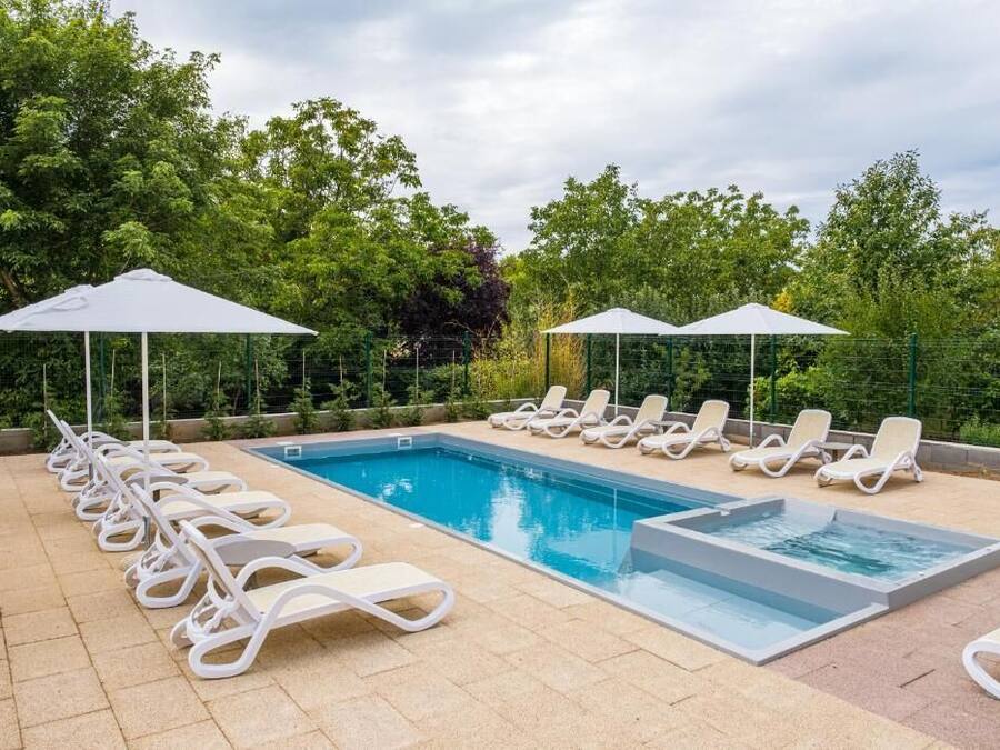 A swimming pool with lounge chairs and umbrellas, surrounded by greenery.
