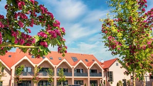 A building with a red-tiled roof and multiple windows, surrounded by a parking lot with several cars. - Kistücsök Food & Room (Balatonszemes)