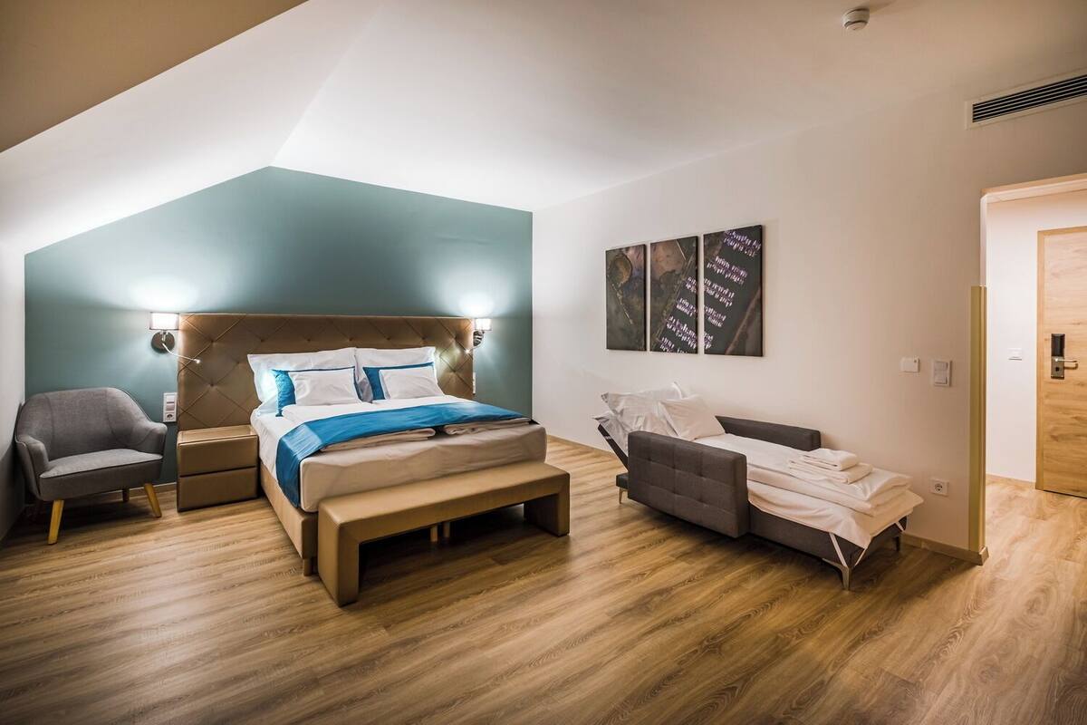 A modern bedroom with a large bed, a bedside table, a chair, and a sofa.