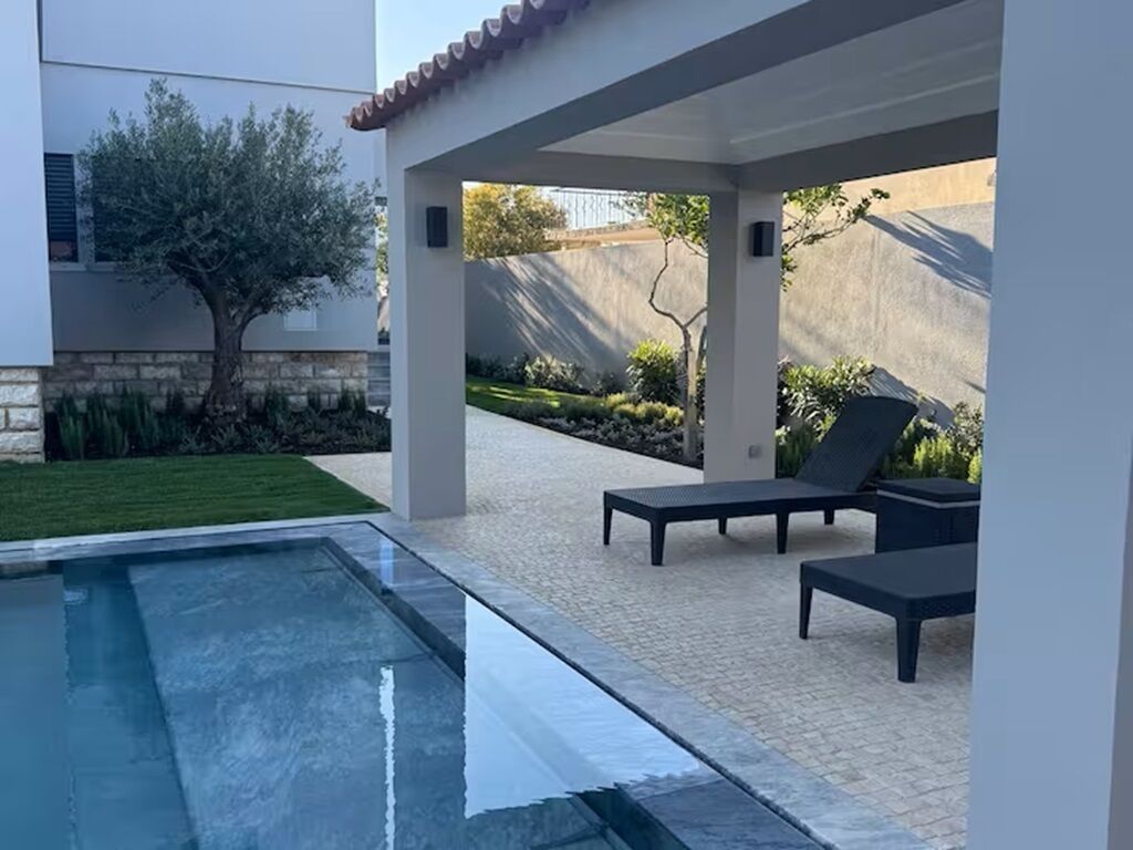 Ein moderner Poolbereich im Freien mit freiem Blick auf den Pool, Liegestühlen und einer Steinmauer im Hintergrund.