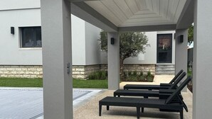 Een overdekt terras met twee lounge fauteuils en een vloer van natuursteen.