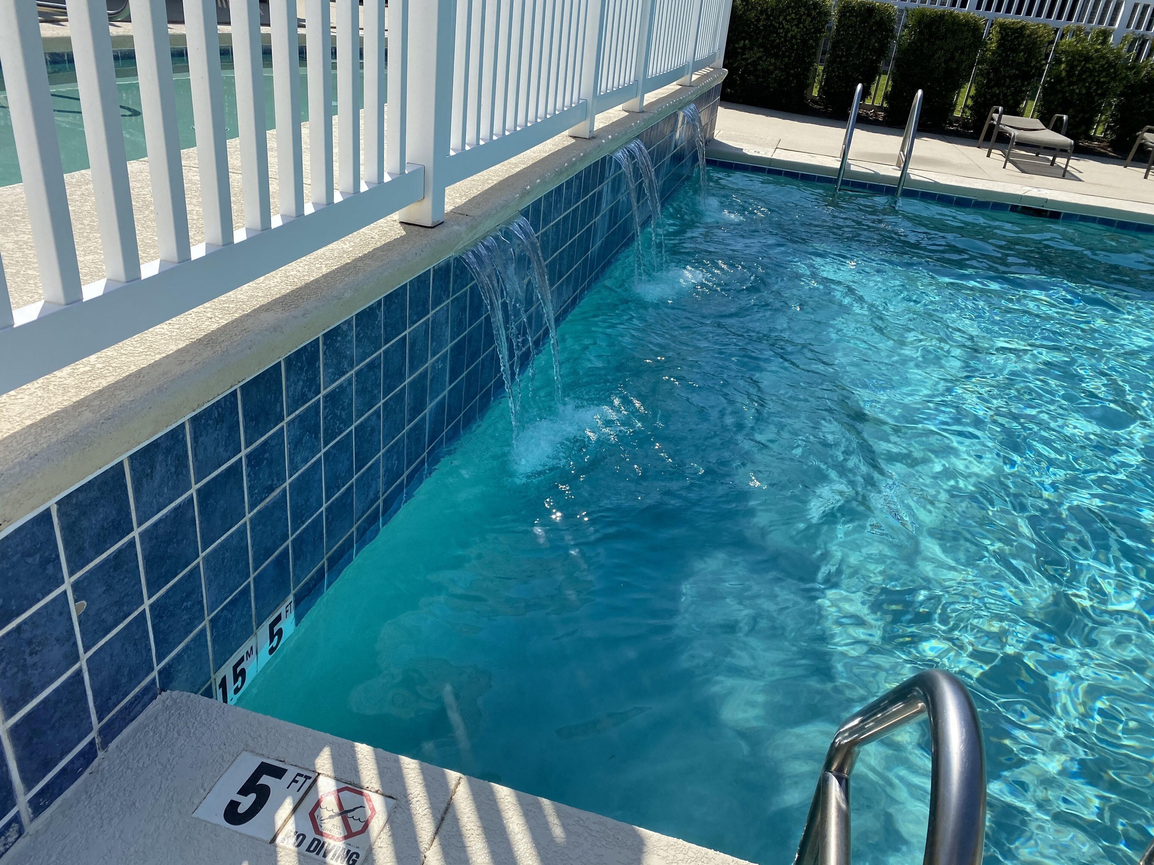 En swimmingpool med en skylt som visar att den är 1,5 meter djup, klart blått vatten och ett vitt staket.