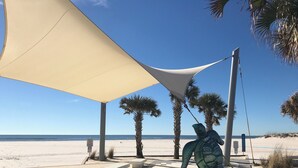 A beachside area with a shaded seating area, palm trees, and a decorative sculpture. - Elegant 3-bedroom condo with 2 King beds/2 twins close to OWA/Foley Sports Plex. (Foley)