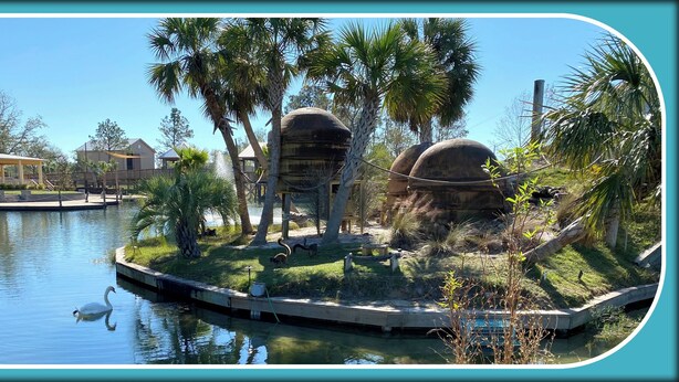 A serene water body with a swan, surrounded by palm trees and a small island with a gazebo. - Elegant 3-bedroom condo with 2 King beds/2 twins close to OWA/Foley Sports Plex. (Foley)