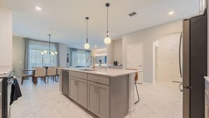 A modern kitchen with a central island, pendant lighting, and a dining area with a table and chairs. - Francheska`s Villa: Private Pool/Spa, 24/7 Support (Davenport)